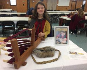 girl showing off an inkle loom and rabbit skin pouch