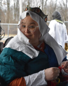 a woman wearing a baronial coronet and a white veil sits holding a needle and thread