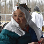 a woman wearing a baronial coronet and a white veil sits holding a needle and thread